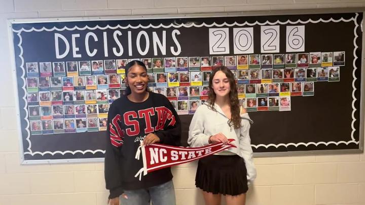 Two Northwest H.S. Seniors stand in front of a college decision day bulletin board