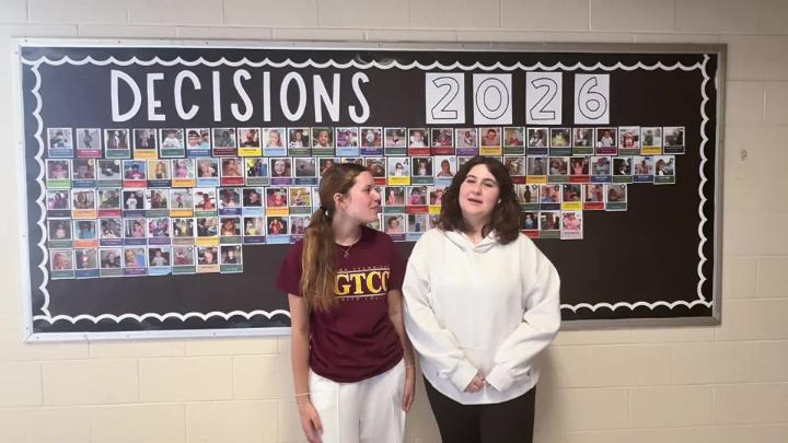 Two Northwest H.S. Seniors stand in front of a college decision day bulletin board