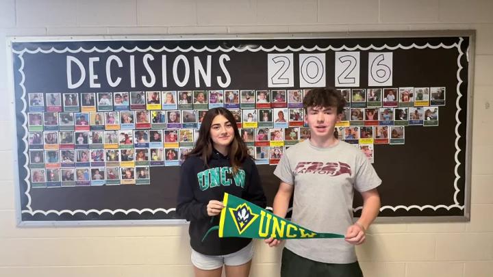 Two Northwest H.S. Seniors stand in front of a college decision day bulletin board