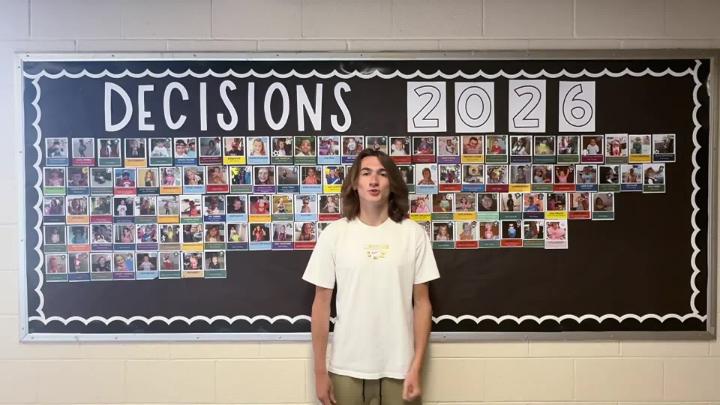 Northwest H.S. senior stands in front of Decision Day 2026 bulletin board